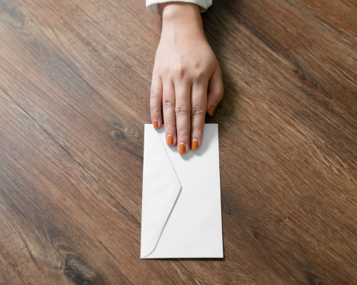 Hand with painted nails sliding a envelope across a wooden table